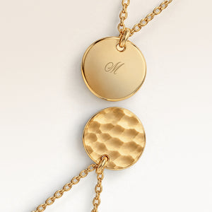 Close-up of two round pendants in gold – rippled front and polished back with an engraved initial
