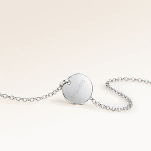 Back of a round silver necklace with a personal engraved date