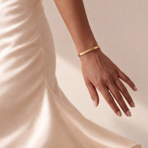Modell i krämfärgad satinklänning med personligt bangle-armband i guld med ingraverat datum