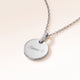 Round silver necklace with zirconia seen from the side with an engraved name and heart