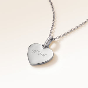 Angled close-up of minimalist heart-shaped heart pendant in silver with white zircons and space for personalized engraving on the front and back