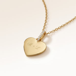 Close-up of minimalist heart-shaped heart pendant in gold with white zircons and space for personalized engraving on the front and back