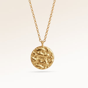 Närbild av minimalistiskt runt berlock i guld med mjukt smält finish och plats för gravyr baktill