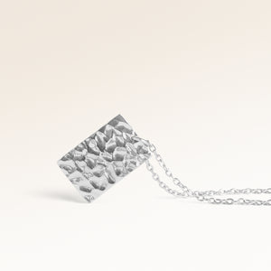 Close-up of minimalist square pendant in silver with rippled wave surface and space for engraving on back