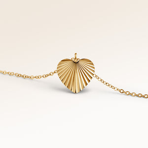 Close-up of minimalist heart pendant in gold with ribbed sunburst surface and space for engraving on the back.