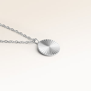 Närbild av minimalistiskt runt berlock i silver med räfflad solstråle-yta och plats för gravyr baktill