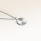 Närbild av minimalistiskt runt berlock i silver med räfflad solstråle-yta och plats för gravyr baktill