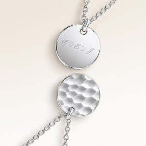Close-up of two round pendants in silver – rippled front and polished back with an engraved initial